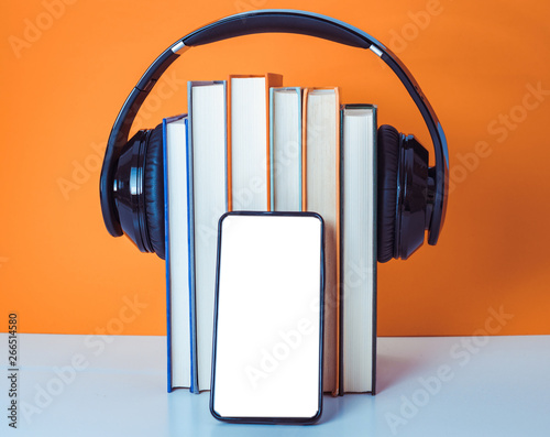 Audiobooks concept. Headphones put over book on orange and white background. Smart phone. Mobile phone.