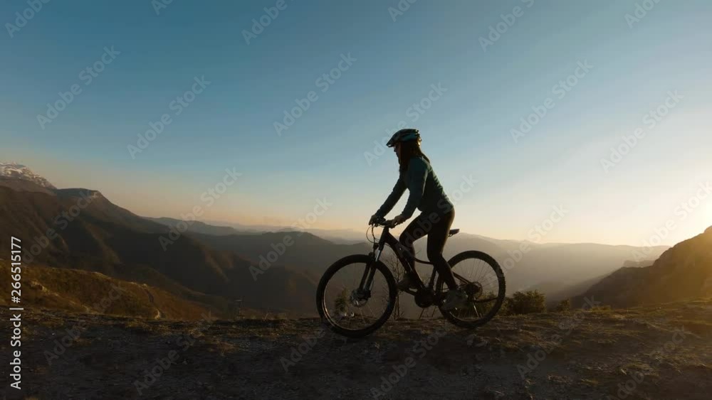 Girl riding her bike at the top of a mountain at sunset. Beautiful canyon lake in the background.