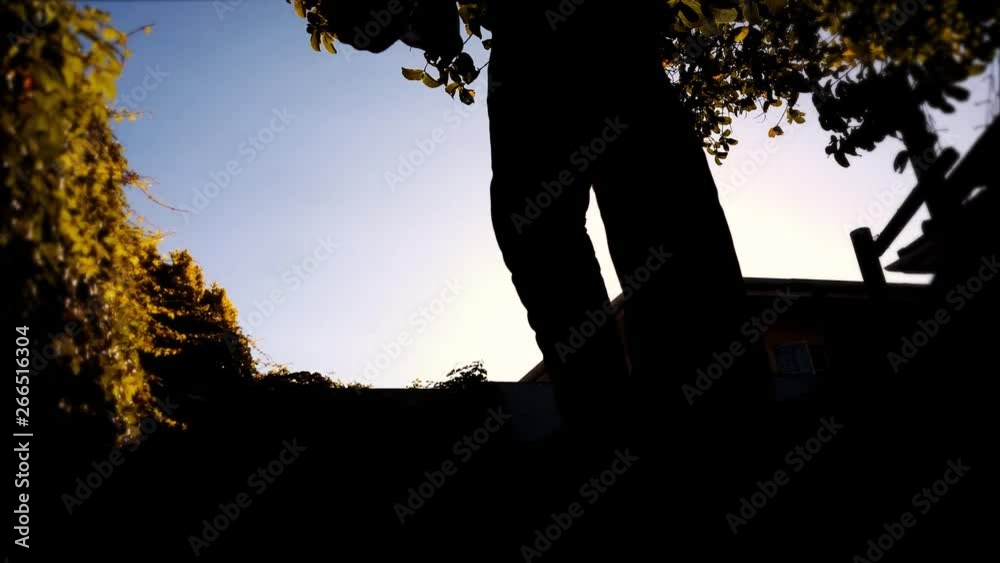 Dark shadow silhouette of male figure closeup digging dirt & throwing it towards camera view. Bright foliage background. Scary, creepy concept or gardening, grave digger burial.