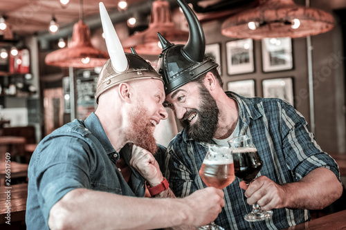 Friends in viking helmets colliding foreheads and clinking glasses.