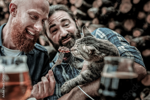 Two kind men feeding a stray cat.