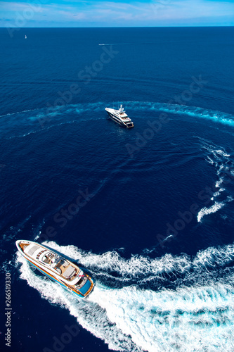 Aerial view of luxury big yachts on sea. Big motor yacht running around the luxury yacht creating circles on the water  © LaptevArt