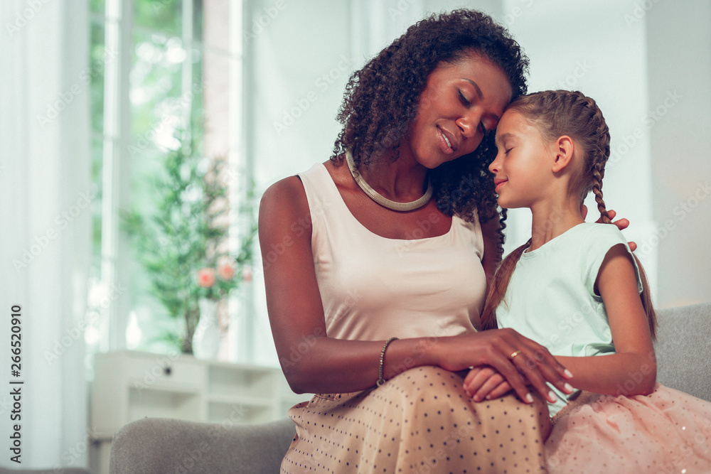 Obraz premium Cute little daughter being hugged by a loving Afro-American mom.