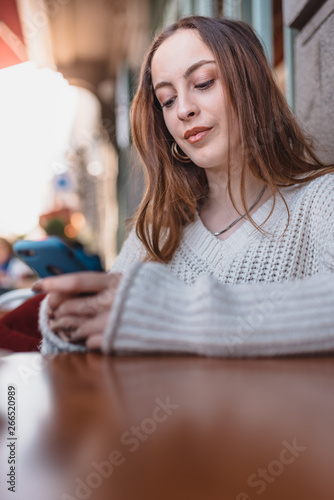 Beautiful young girl in outdoor uses smart phone and texting