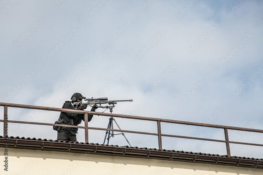 Police sniper aiming with optical sight from roof