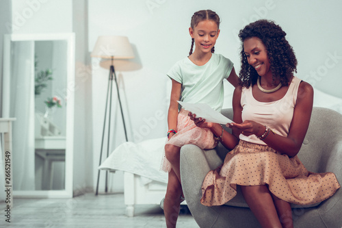 Glowing Afro-American mother looking at the drawing of daughter. photo