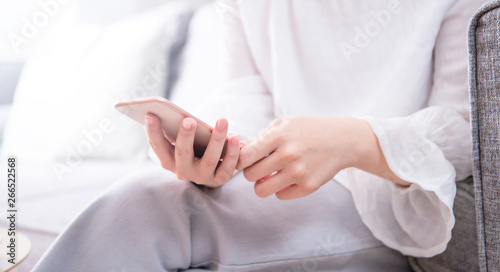 Side view of asia young woman in white sitting on sofa and using smart phone in bright living room  copy space  close up  blank for design concept