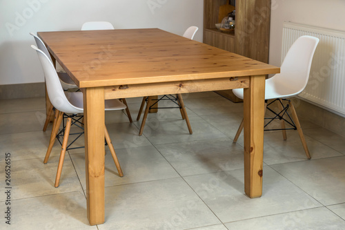 Massive kitchen table with chairs in the interior with beige tiled floor.