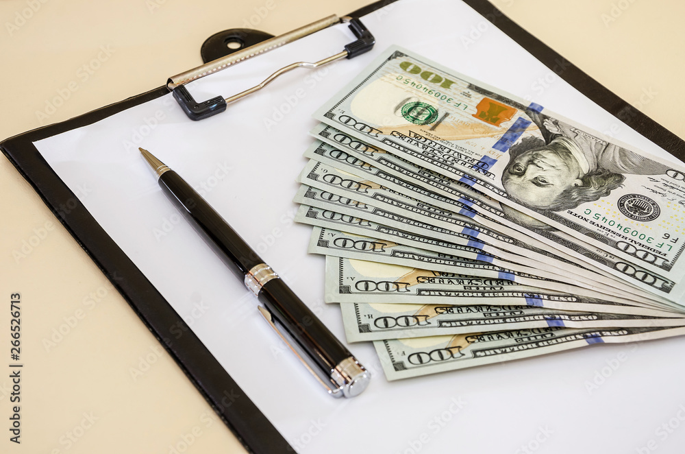Dollars, pen and white sheet of paper on the background of the table. Close-up. Dollars, pen and white sheet of paper on the background of the table. Close-up.