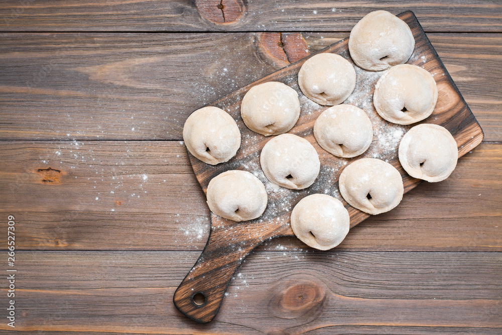 Raw dumplings ready for cooking lie in rows on a wooden cutting board on the table. Top view. Copy space Raw dumplings ready for cooking lie in rows on a wooden cutting board on the table. Top view. Copy space