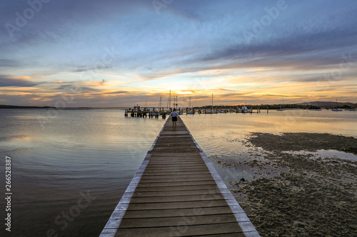 Timber jetty leading to sun setting over ocean © jmimages