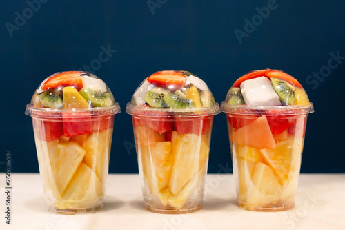 Three mixed fruit vitamin salad in the plastic glass ready to takeaway. Kiwi, pineapple, watermelon, coconut, strawberry, mango in plastic container. Copy space.