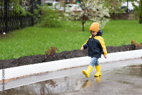 little boy walks through the puddles in the spring after the rain