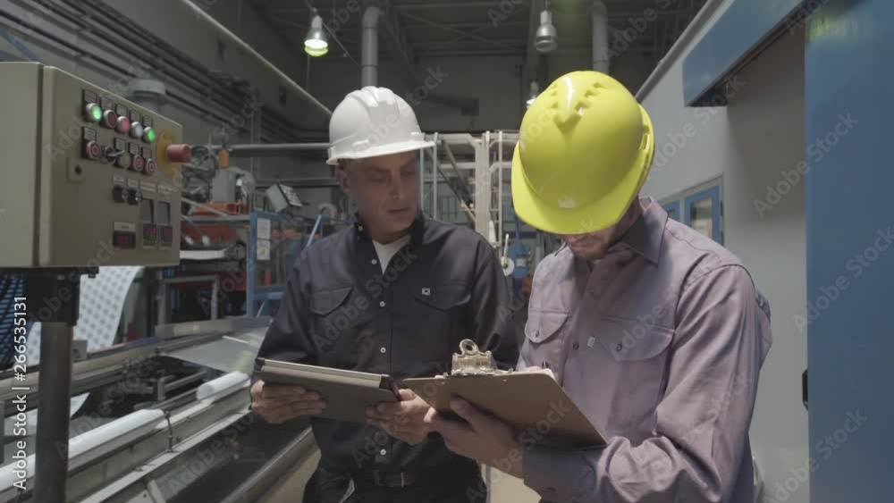 Medium shot of engineer and coworker using clipboard and digital tablet while monitoring control panel in factory