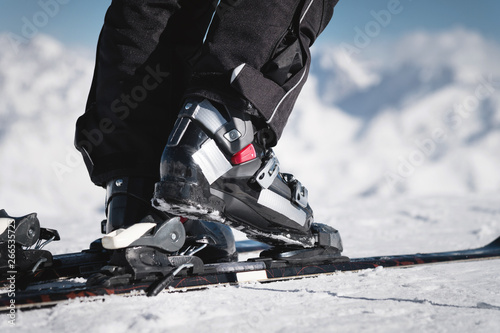 Close-up of the athlete's skier's foot in ski boots rises into the skis against the background of the snow-capped Caucasus mountains on a sunny day. Winter sports concept photo