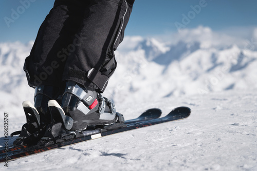 Close-up of the athlete's skier's foot in ski boots rises into the skis against the background of the snow-capped Caucasus mountains on a sunny day. Winter sports concept photo