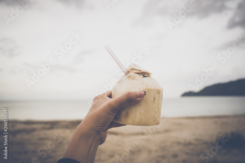 Close up hand woman holding coconut on the beach background. Vintage or rettro tone. photo