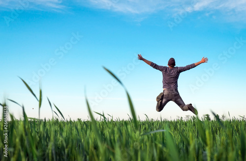 Young man jumping for joy over a green wheat field. Handsome farmer. Spring agriculture. Man admires the beauty of nature