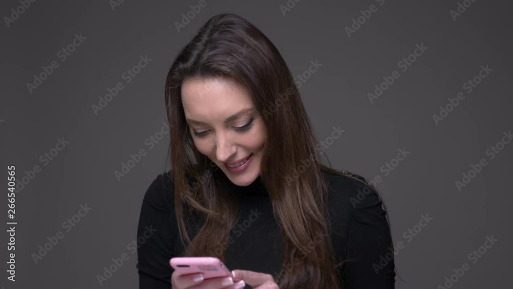 Closeup portrait of adult attractive caucasian female using the phone smiling happily with background isolated on gray