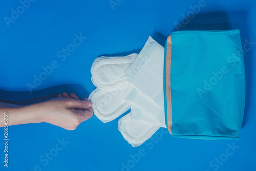 Young women taking sanitary pads inside of her cosmetic bag on blue background