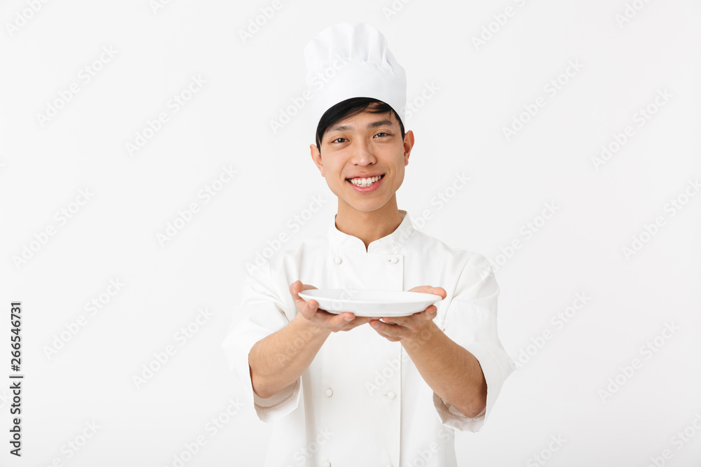 Image of asian positive chief man in white cook uniform smiling at camera while holding a plate Image of asian positive chief man in white cook uniform smiling at camera while holding a plate