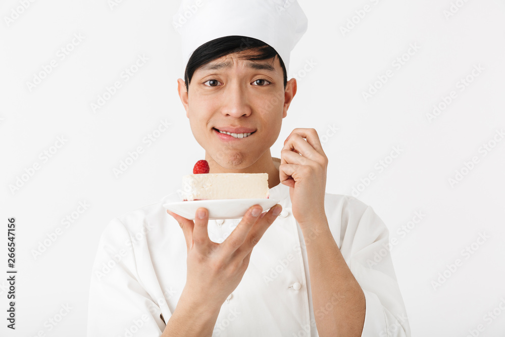 Image of positive chinese chief man in white cook uniform smiling at camera while holding platter with tasty cheesecake Image of positive chinese chief man in white cook uniform smiling at camera while holding platter with tasty cheesecake