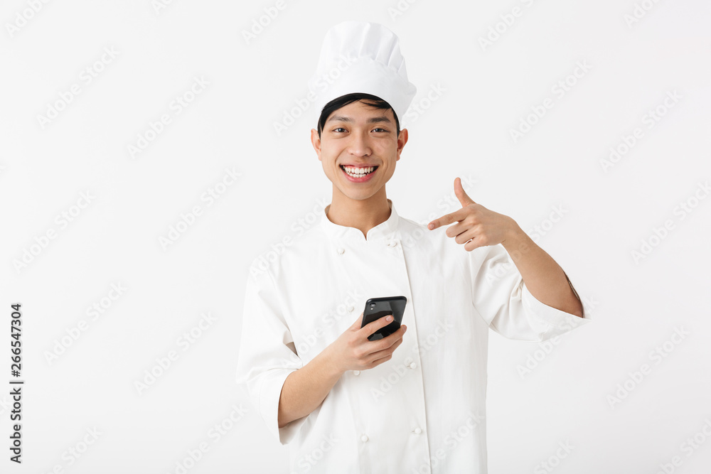 Image of positive chinese chief man in white cook uniform and chef's hat holding mobile phone Image of positive chinese chief man in white cook uniform and chef's hat holding mobile phone