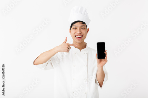Image of smiling chinese chief man in white cook uniform and chef's hat holding mobile phone