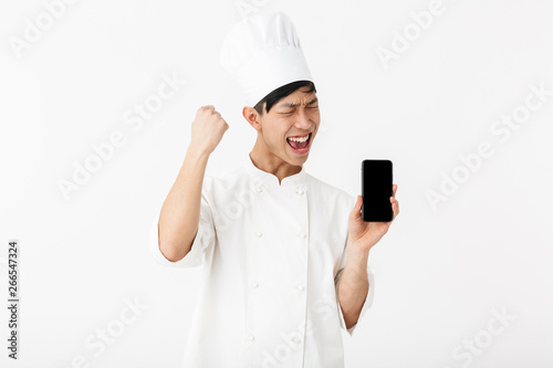 Image of handsome chinese chief man in white cook uniform and chef's hat holding mobile phone