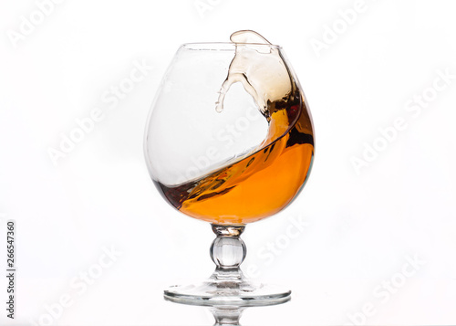 splash of brown alcohol drink in crystal glass on white background with reflection