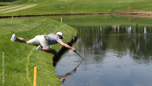 A golfer reaches into a pond to retrieve his ball