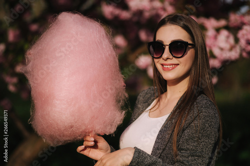 Close up portrait of smiling girl holding cotton candy in hands. Girl dressed in grrey blazer and sunglasses photo