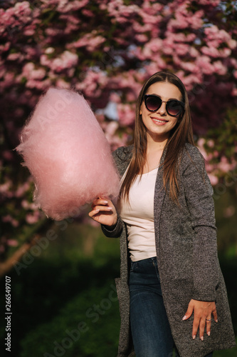 Close up portrait of smiling girl holding cotton candy in hands. Girl dressed in grrey blazer and sunglasses photo