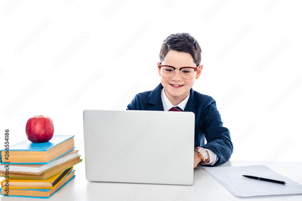 schoolboy in glasses sitting at desk with books and using laptop isolated on white schoolboy in glasses sitting at desk with books and using laptop isolated on white