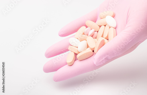 tablets lie on the palm. Hand in pink glove holds pills