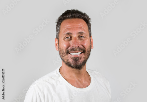 portrait of young happy and attractive man with blue eyes and beard looking cool smiling happy and confident wearing white t-shirt isolated on studio background