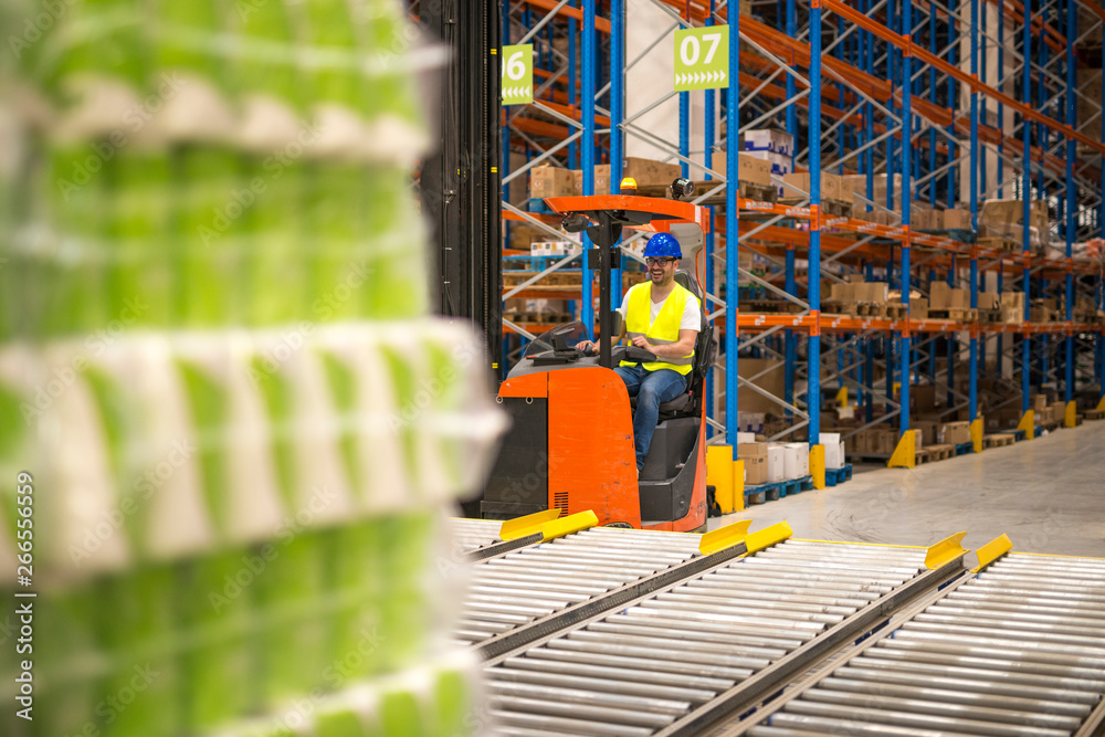 Forklift driver handling goods in big warehouse distribution center.