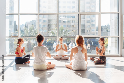 Stylish young women meditate in padmasana sitting on the floor in a bright gym with large windows. Concept of maintaining of freshness of mind and eliminating lethargy and drowsiness