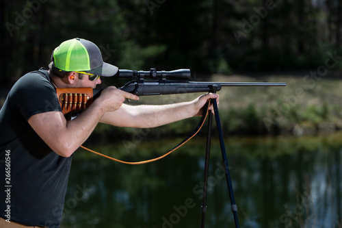 A man aiming a hunting rifle resting on shooting sticks.