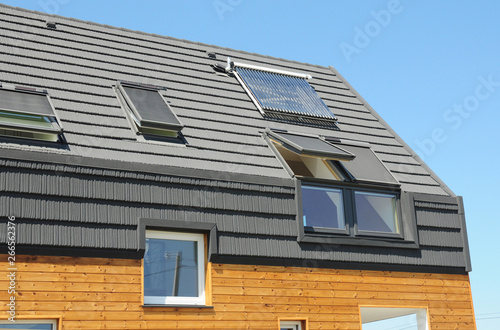 Modern passive house roof with attic skylight windows, solar water heater, solar panels, asphalt shingles.