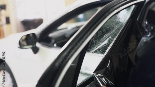 Close-up worker installs tint film for car glass, slow-motion.