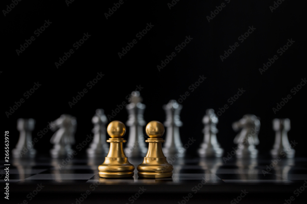 Two golden chess pawns are facing silver chess on black background. Business partnership concept.