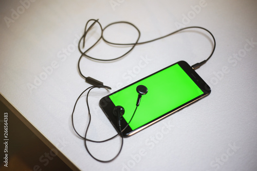 Smartphone Green Screen and Black Earphones on white table