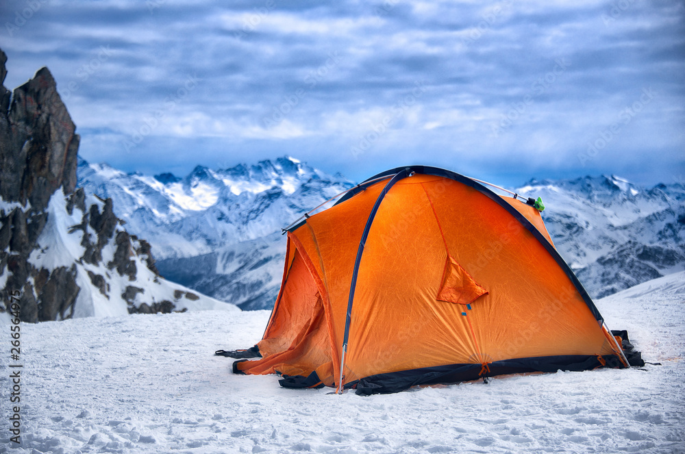 Red orange tent in a solitary bivouac in the snow atop a mountain (Mont Blanc in the Alps between Italy and France) with a view of the mountain range under an overcloud sky
