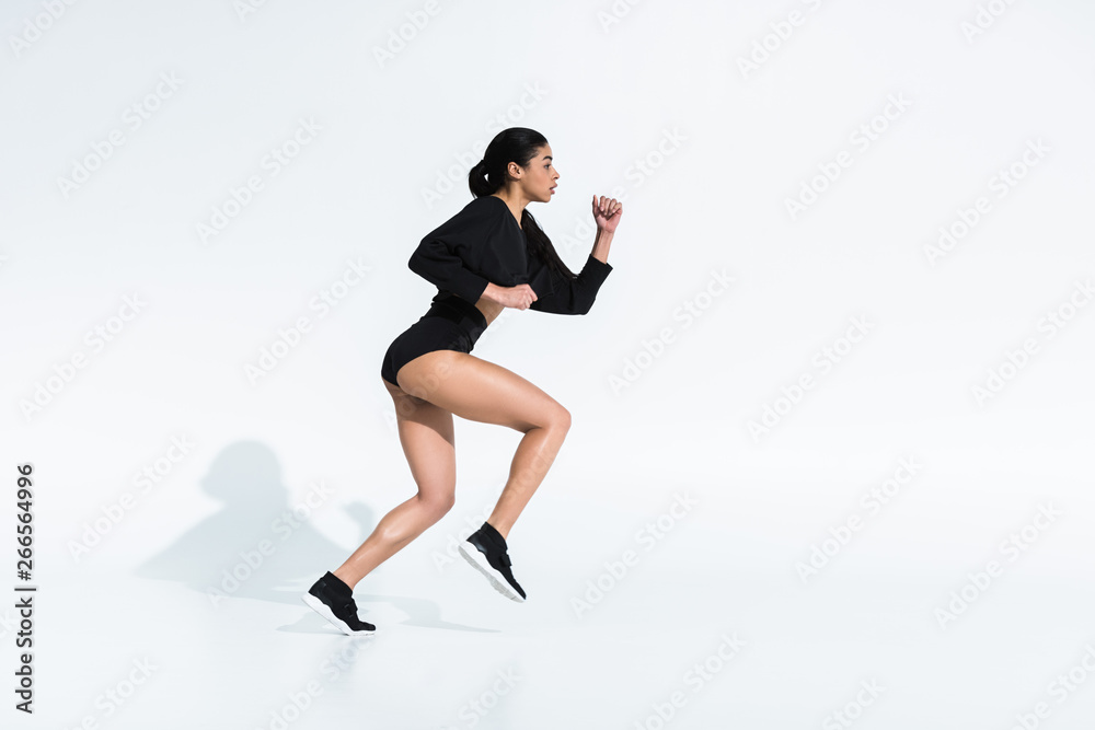 side view of beautiful sportive african american girl in black sportswear running on white side view of beautiful sportive african american girl in black sportswear running on white