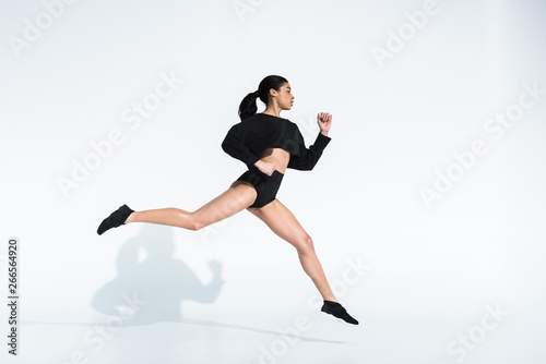 side view of sportive african american girl in black sportswear and sneakers running on white