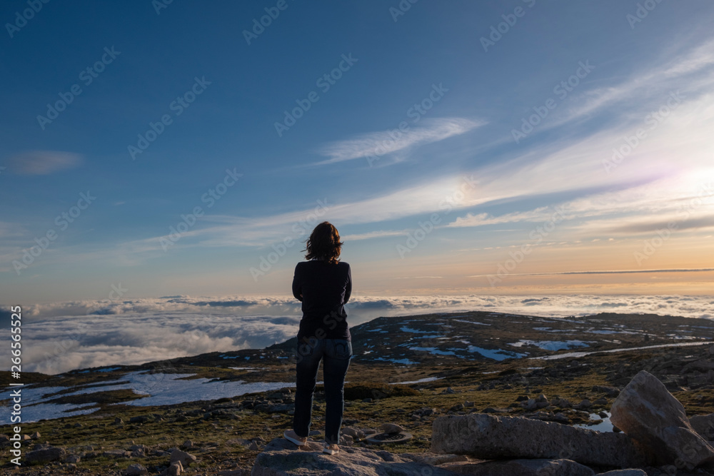 Amazing sunset view above clouds, with Young Woman Contemplating it, from Torre (Tower) The Highest Point in Portugal, Serra da Estrela, Portugal
