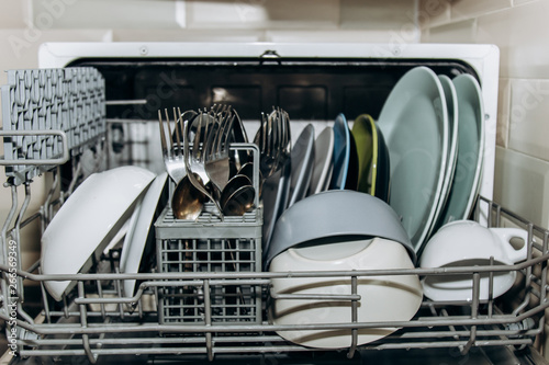open dishwasher close up clogged with clean washed dishes. dry cutlery closeup. spoons forks. mugs, plates. household appliances in the kitchen