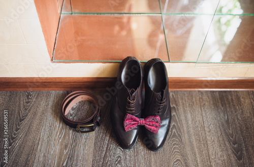 Wedding arrangement and concept. Shoes, red bowtie and leather belt lie on the background of the parquet. Morning groom.