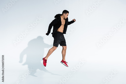 handsome mixed race man in black sports jacket, shorts and red sneakers jumping on white